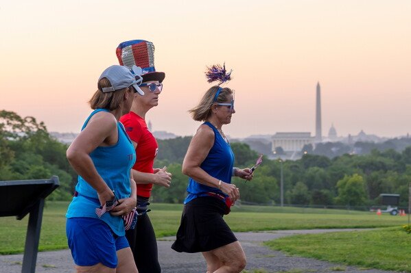 Runners wearing Independence Day-themed items jog at dawn past an overlook in Arlington, Va., as Washington prepares for sweltering temperatures, Friday, July 3, 2026. (AP Photo/J. Scott Applewhite)