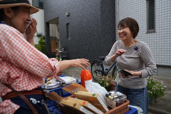 Akiko Sugaya, left, chats with her regular customer buying her items, while she peddles tofu, prepared food and beverages in a cart in Tokyo, Saturday, July 4, 2026. (AP Photo/Hiro Komae)
