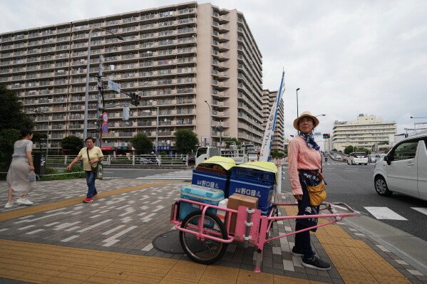 Akiko Sugaya waits at a traffic intersection while she peddles tofu, prepared food and beverages in a cart in Tokyo, Saturday, July 4, 2026. (AP Photo/Hiro Komae)