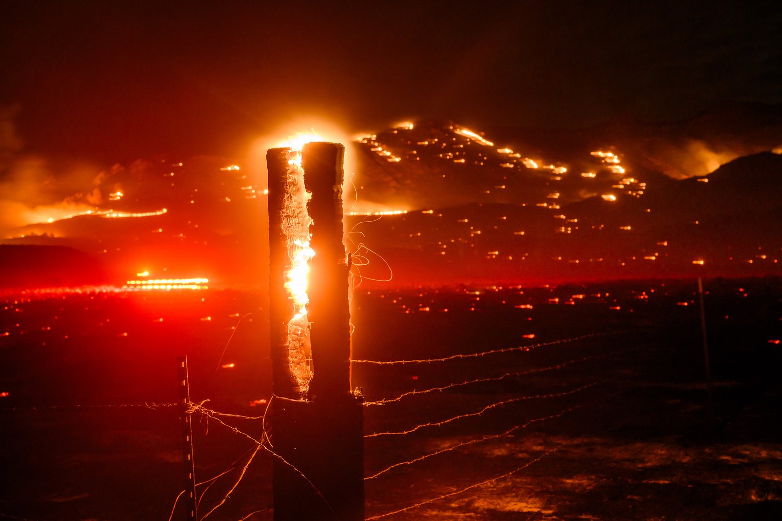 Seen in a long exposure, flames consume a fencepost as the Bug Fire burns near Doyle in unincorporated Lassen County, Calif., on Thursday, Aug. 13, 2026. (AP Photo/Noah Berger)