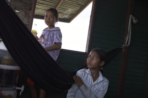 Sou Sreynich, 13, and her younger sister at their home in one of the floating villages of Cambodia's Tonle Sap Lake on Monday, June 29, 2026. (AP Photo/Aniruddha Ghosal)