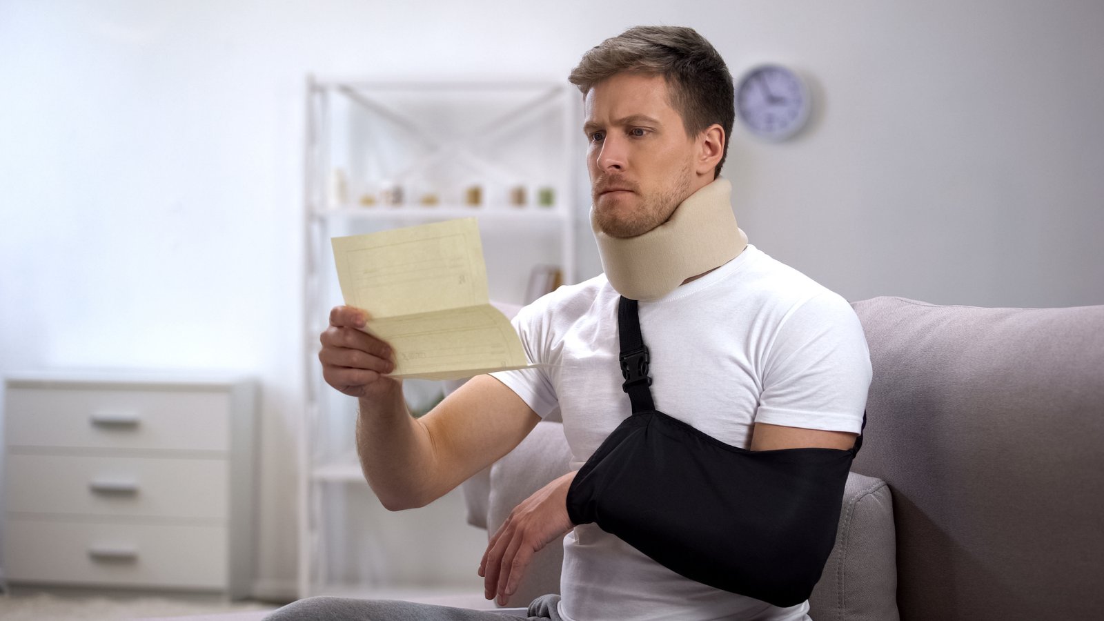 Man in cervical collar and arm sling looks shocked while reading a medical bill.